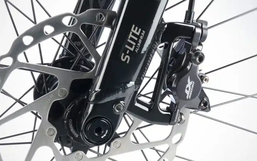 Detailaufnahme der Vorderradbremse eines STEVENS 6X Lite Tour LT Trekkingrads, mit Fokus auf die Shimano Deore Scheibenbremse und die S-Lite Aluminiumgabel.