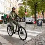 Frau in Freizeitkleidung mit Helm fährt ein Stevens Aviolo 5.2 HT Tourenrad über einen Zebrastreifen in einer deutschen Stadt.