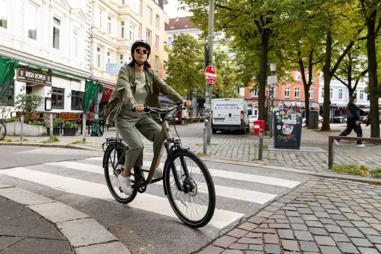 Frau in Freizeitkleidung mit Helm fährt ein Stevens Aviolo 5.2 HT Tourenrad über einen Zebrastreifen in einer deutschen Stadt.