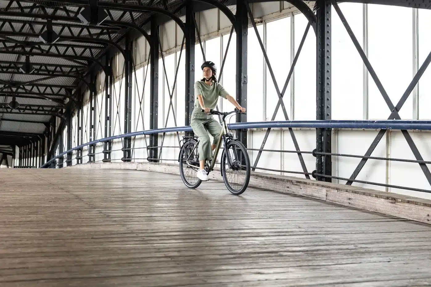 Eine Frau mit Helm fährt ein Stevens Aviolo 5.2 HT Tourenrad auf einer Holzbrücke.