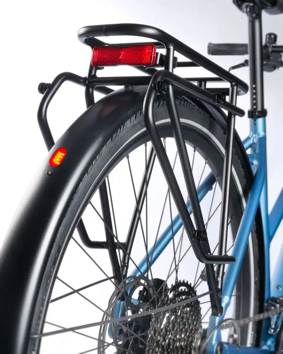 Nahaufnahme des Hinterrads eines blauen STEVENS Aviolo 8.1 LT Trekkingrades. Abgebildet sind der schwarze Gepäckträger mit integriertem Rücklicht, das Schutzblech mit zusätzlichem Reflektor und die Kette mit der Kassette der Gangschaltung.