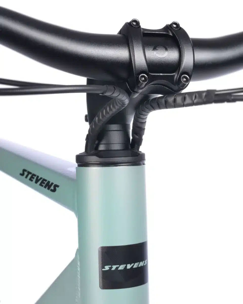 Detailaufnahme des Vorderbaus eines mintgrünen Stevens Caleta 6.1 HT Fahrrads, Fokus auf Lenker, Vorbau und Steuerrohr mit Kabeln.