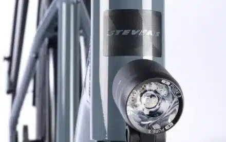 Detailaufnahme der runden, schwarzen Supernova E3 Pure 3 Frontleuchte mit sichtbaren LEDs, montiert an der Gabel eines grauen Stevens Caleta 8.2 LT Fahrradrahmens.