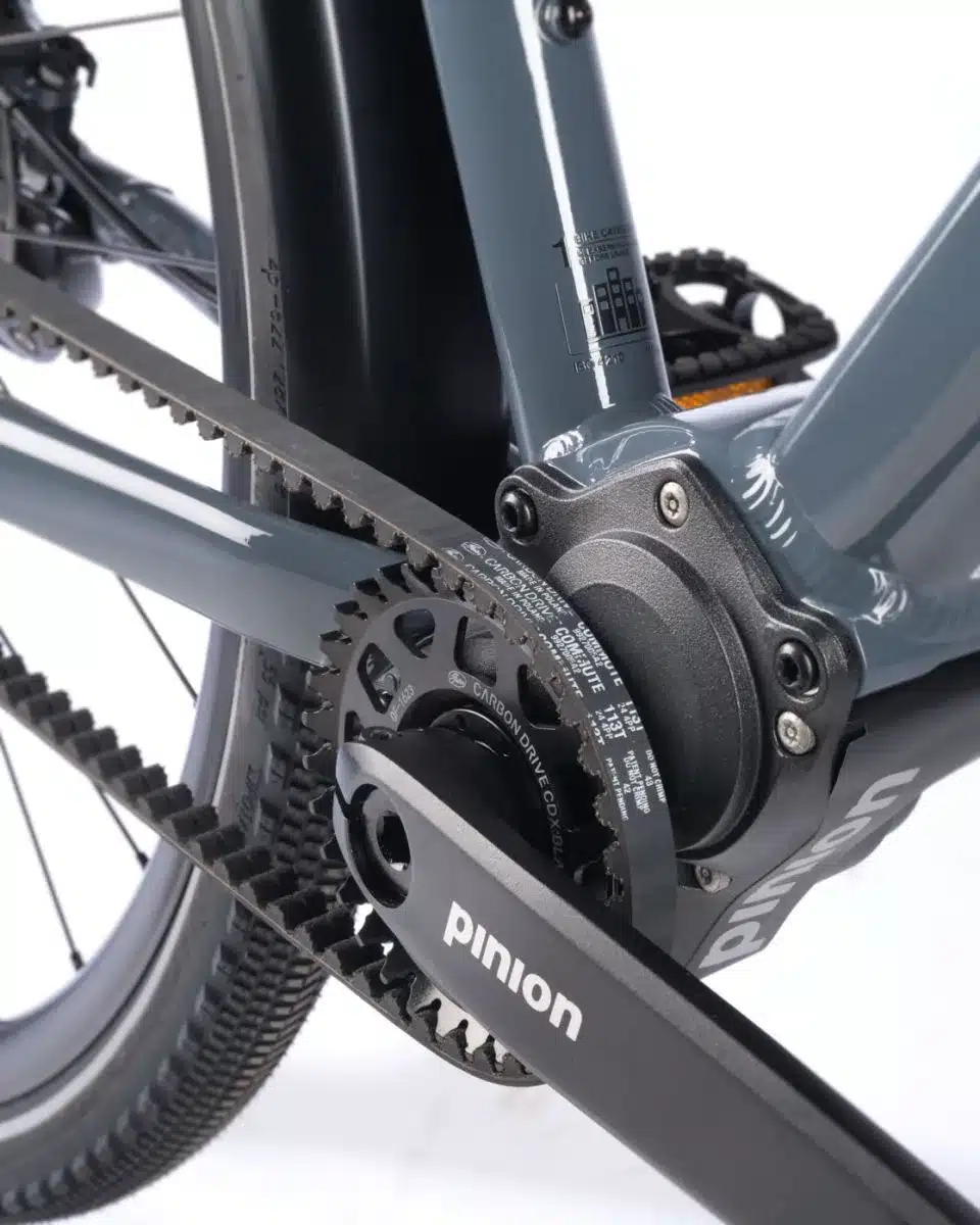 Nahaufnahme des Antriebsstrangs eines Stevens Caleta 8.2 LT Fahrrads, das ein Pinion C1.12 Getriebe und einen Gates Carbon Drive Riemen zeigt.