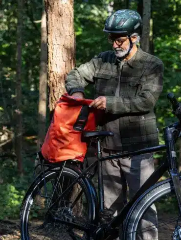 Ein Mann bereitet sein Stevens Caleta 9.2 LT Trekkingrad für eine Tour vor, indem er eine Tasche auf den Gepäckträger lädt.