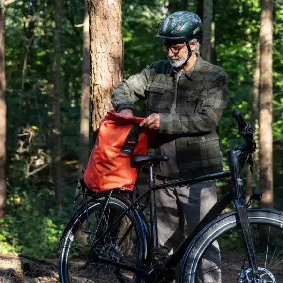 Ein Mann bereitet sein Stevens Caleta 9.2 LT Trekkingrad für eine Tour vor, indem er eine Tasche auf den Gepäckträger lädt.