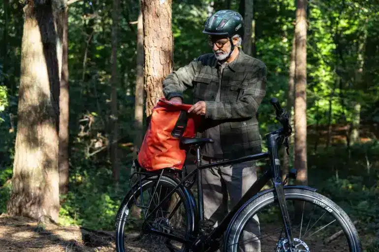Ein Mann bereitet sein Stevens Caleta 9.2 LT Trekkingrad für eine Tour vor, indem er eine Tasche auf den Gepäckträger lädt.