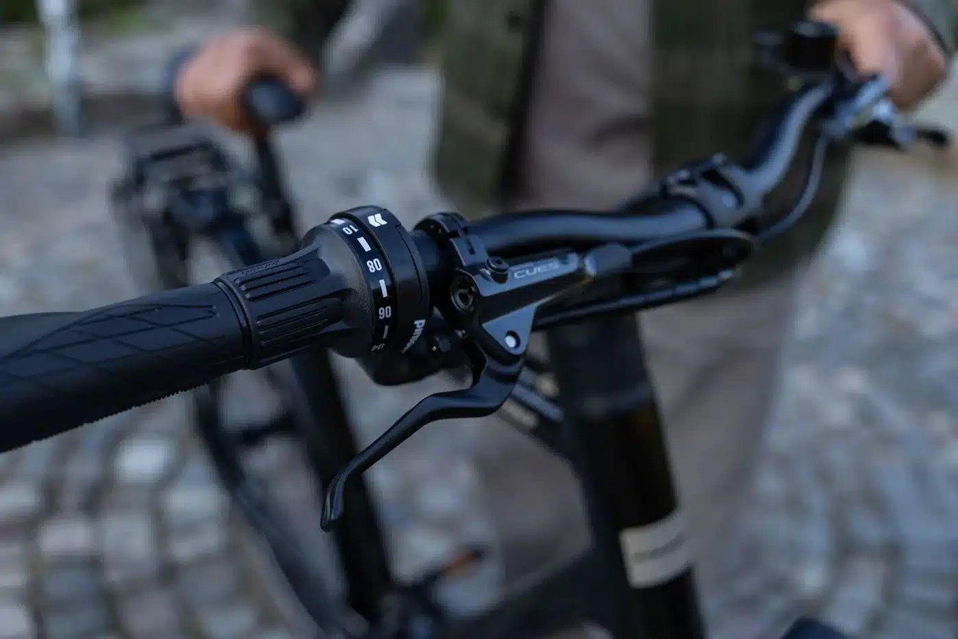 Nahaufnahme des Lenkers eines Stevens Caleta 9.2 LT Fahrrads mit Fokus auf den Drehgriffschalter und den Bremshebel. Auf dem Drehgriff sind Gangstufen mit Zahlen wie 80 und 90 erkennbar, was auf ein Pinion-Getriebe hindeutet.