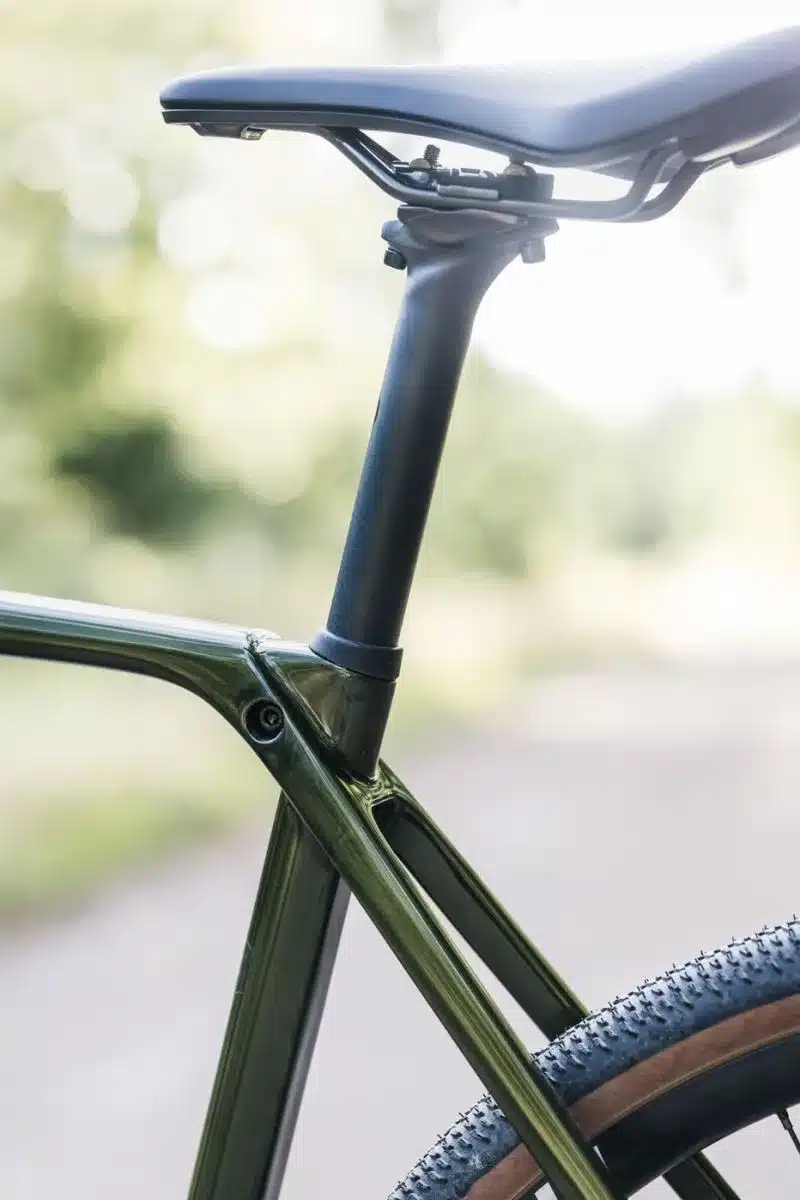 Detailansicht des dunklen Carbon-Sattelstütze des Stevens Camino RS, montiert an einem grünen Carbonrahmen, mit Fokus auf den Übergangsbereich und dem angedeuteten Hinterrad.