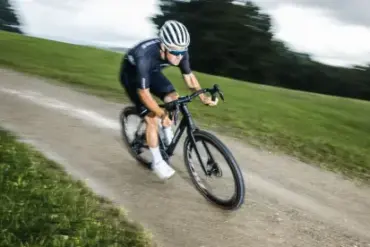 Ein Rennradfahrer fährt mit einem schwarzen Stevens Camino RS Pro AXS Gravelbike auf einem Schotterweg in hügeliger Landschaft.