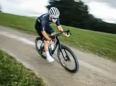 Ein Rennradfahrer fährt mit einem schwarzen Stevens Camino RS Pro AXS Gravelbike auf einem Schotterweg in hügeliger Landschaft.