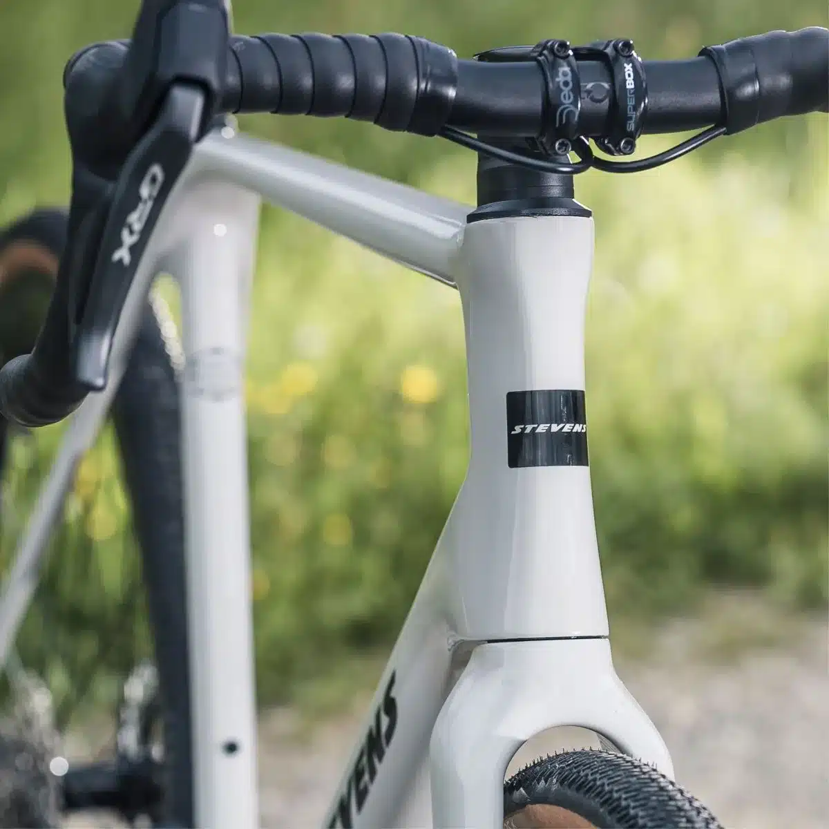 Nahaufnahme eines weißen Gravelbikes des Modells Stevens Camino RS Pro Di2. Man sieht das Steuerrohr mit dem Stevens-Logo sowie den Lenker mit dem Shimano GRX Di2 Schalthebel.