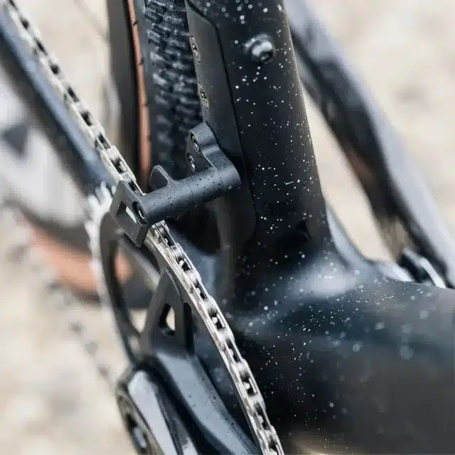 Detaillierte Ansicht des Antriebsstrangs eines Stevens Camino RS Pro Di2 Gravelbikes, Fokus auf Kette und Befestigung des Umwerfers am mattschwarzen Carbonrahmen.