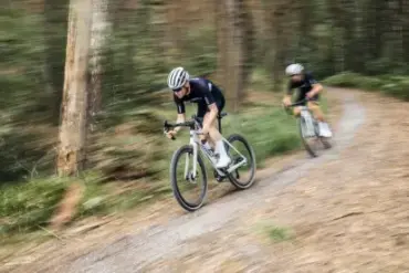 Zwei Radfahrer auf einem Stevens Camino RS Pro Di2 Gravelbike fahren auf einem schmalen Schotterweg durch einen Wald, die Bewegung ist durch eine leichte Bewegungsunschärfe dargestellt.