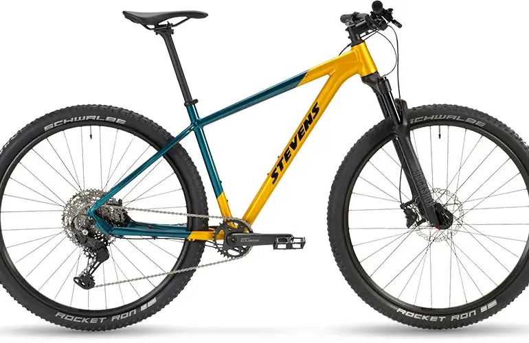 Seitenansicht eines Stevens Devil's Trail Mountainbikes in Gelb-Türkis mit schwarzen Reifen und Federgabel.