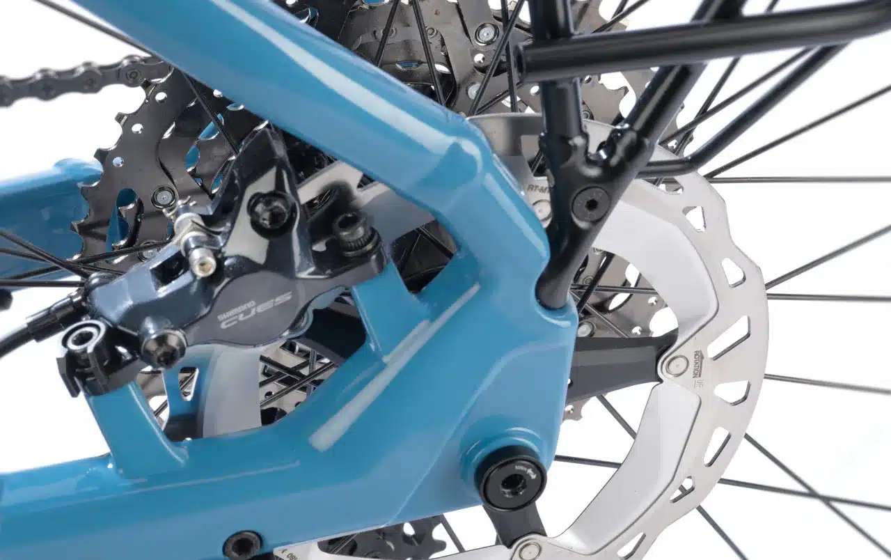 Nahaufnahme des Hinterradbereichs eines blau lackierten STEVENS E-8X Tour Plus HT E-Bikes, mit Fokus auf die Shimano CUES Bremsanlage und die MTB-Kassette.