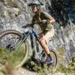 Frau fährt Stevens E-Agnello 7.8.1 E-Mountainbike bergauf auf felsigem Trail.