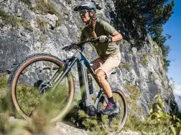 Frau fährt Stevens E-Agnello 7.8.1 E-Mountainbike bergauf auf felsigem Trail.