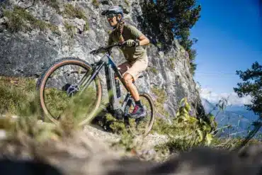 Frau fährt ein Stevens E-Agnello 7.8.1 E-Mountainbike auf einem felsigen Trail mit Blick auf Berge.