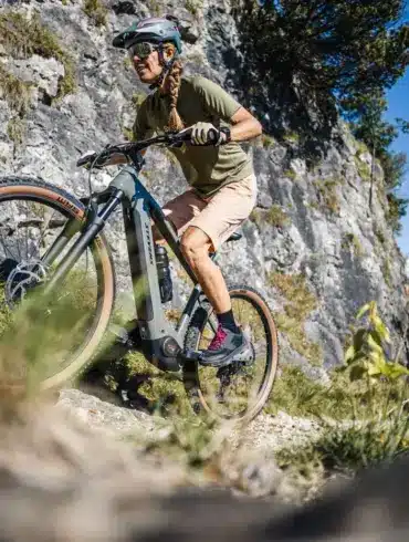 Frau fährt ein Stevens E-Agnello 7.8.1 E-Mountainbike auf einem felsigen Trail mit Blick auf Berge.