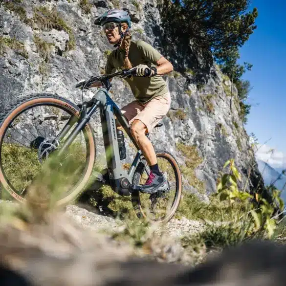 Frau fährt ein Stevens E-Agnello 7.8.1 E-Mountainbike auf einem felsigen Trail mit Blick auf Berge.