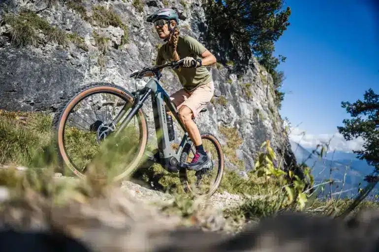 Frau fährt ein Stevens E-Agnello 7.8.1 E-Mountainbike auf einem felsigen Trail mit Blick auf Berge.