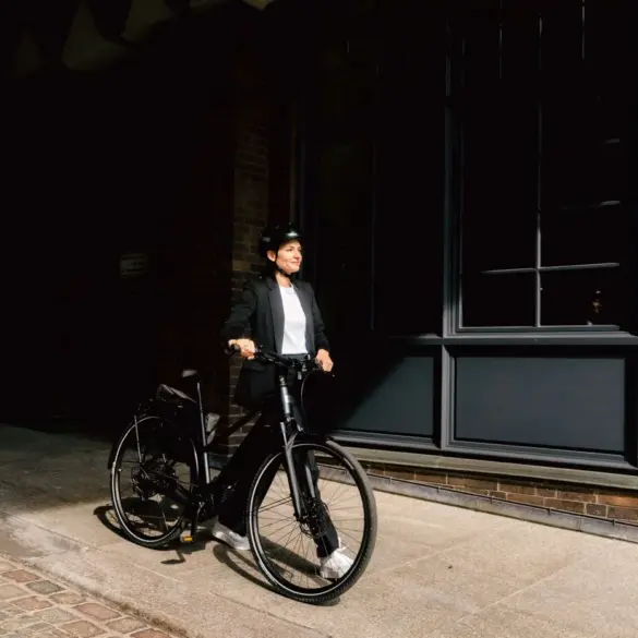 Elektrorad Stevens E-Comuna 7.4.1 HT, schwarz, mit Frau in Business-Kleidung und Helm, bereit für die Fahrt.