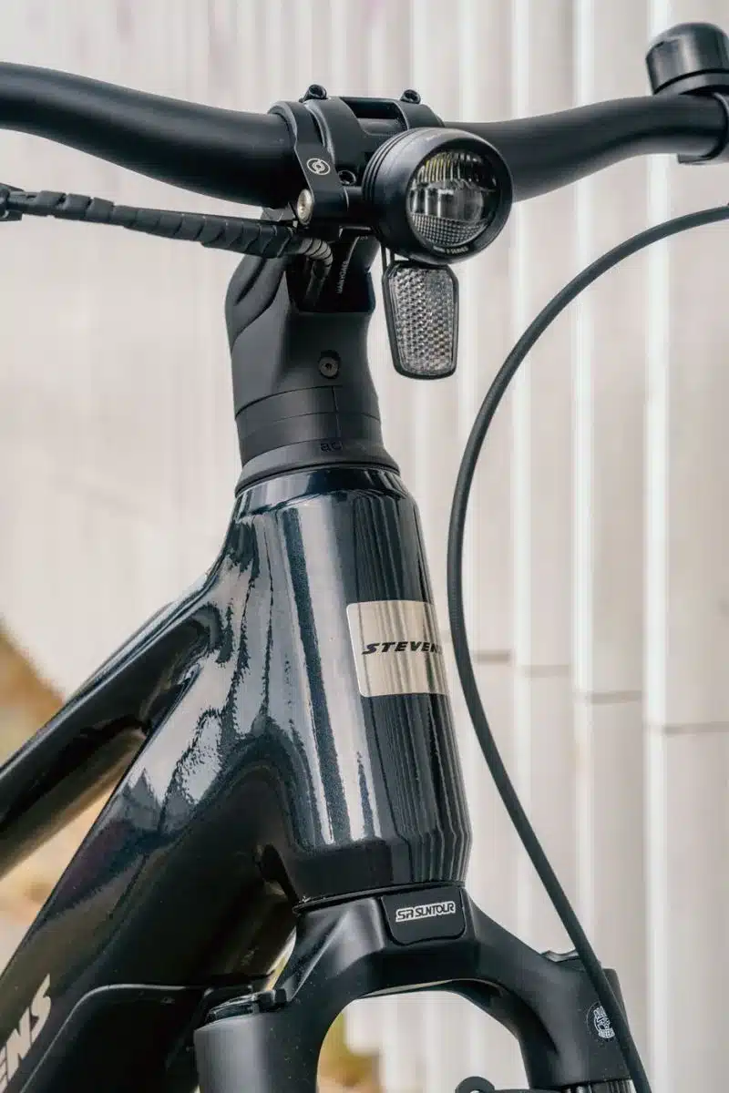 Vorderansicht des schwarzen Stevens E-Comuna 7.4.1 HT E-Bikes mit Fokus auf den Lenker, den Scheinwerfer, das Stevens-Logo und die vordere Federgabel.