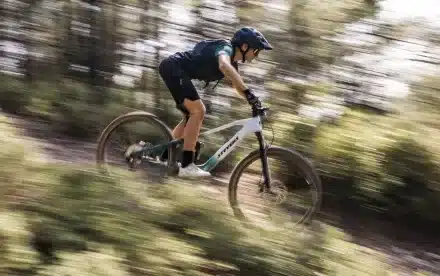 Eine Frau fährt mit einem Stevens E-Maverick AM 7.4.3 Mountainbike auf einem Trail durch einen Wald.