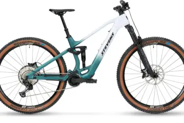 Seitenansicht des Stevens E-Maverick AM 7.4.3, einem weißen und türkisfarbenen E-Mountainbike mit Carbonrahmen und braunen Reifen.