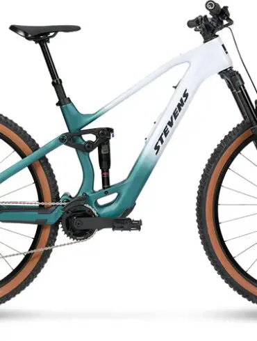 Seitenansicht des Stevens E-Maverick AM 7.4.3, einem weißen und türkisfarbenen E-Mountainbike mit Carbonrahmen und braunen Reifen.