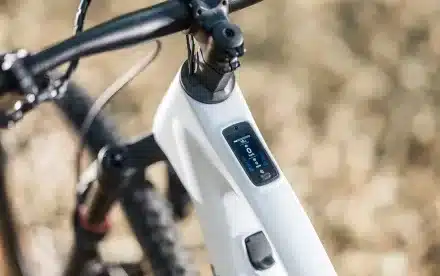 Detailaufnahme des oberen Rahmenteils eines weißen Stevens E-Maverick AM 7.4.3 E-Bikes mit Fokus auf dem integrierten digitalen Display und dem Lenker.