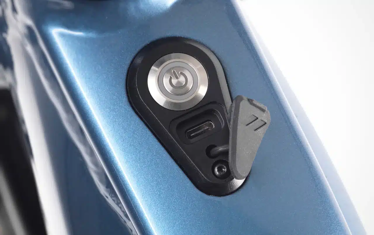 Detailaufnahme des blauen Rahmens eines Stevens E-Triton 7.7.1 E-Bikes, das eine integrierte USB-C-Ladebuchse und den Power-Button zeigt.