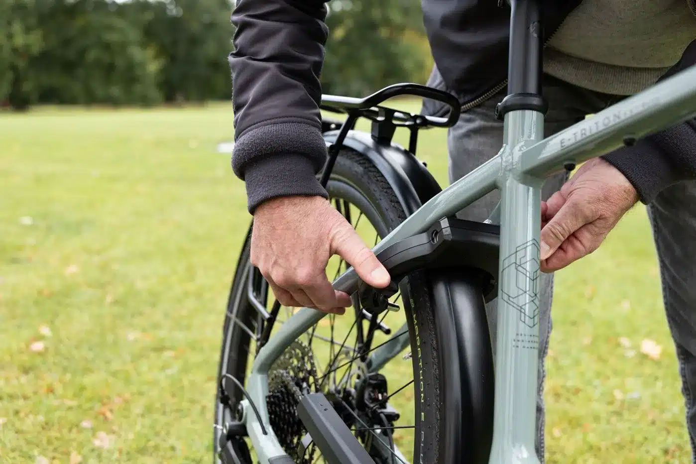 Nahaufnahme eines Mannes, der am Rahmen eines Stevens E-Triton 7.8.1 Plus Forma E-Bikes eine Einstellung vornimmt, mit Fokus auf das Hinterrad und den Gepäckträger.