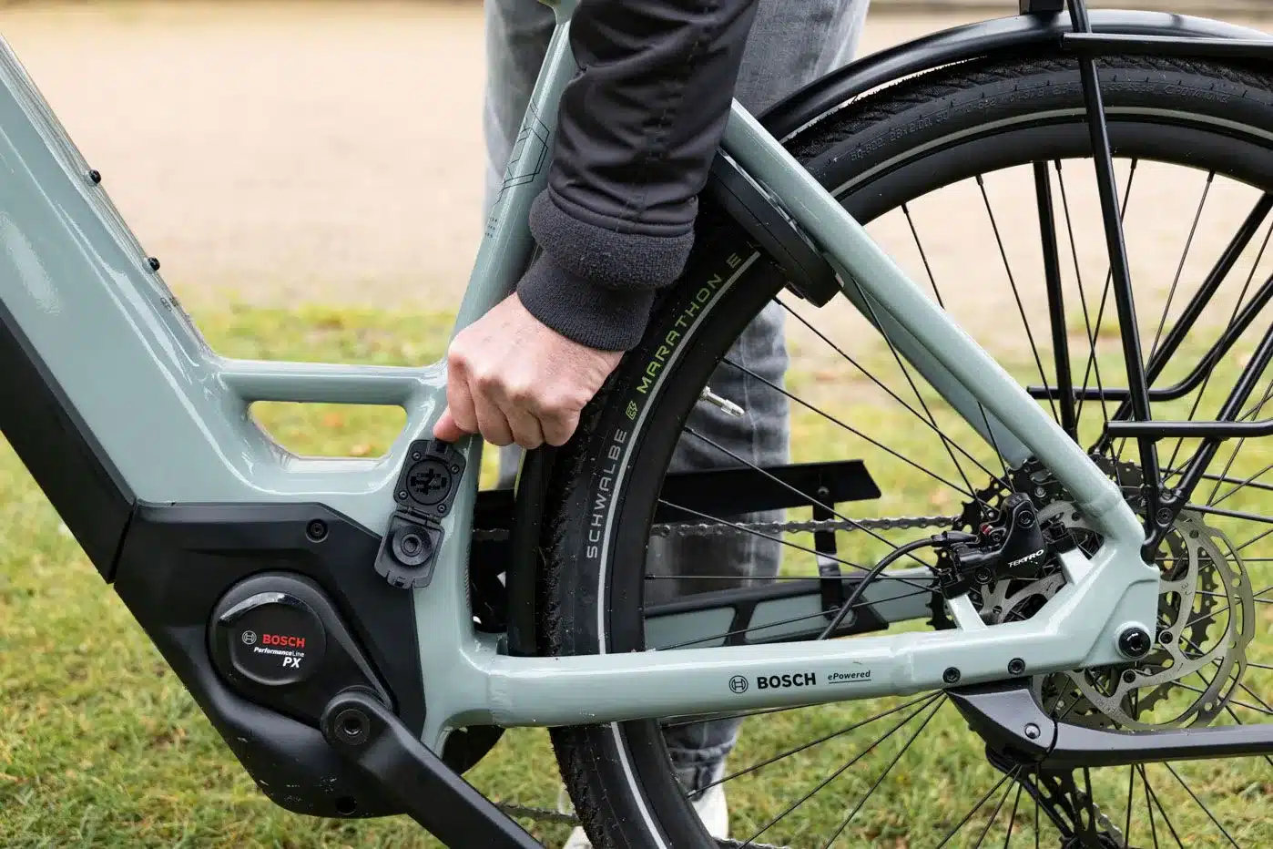 Nahaufnahme des Ladeanschlusses und des Hinterrads eines grauen E-Bikes mit Bosch Motor.