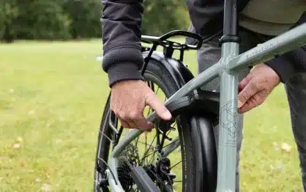 Detailansicht des Rahmens eines grünen STEVENS E-Tourers mit Gepäckträger und Schutzblech, während eine Person etwas daran befestigt.