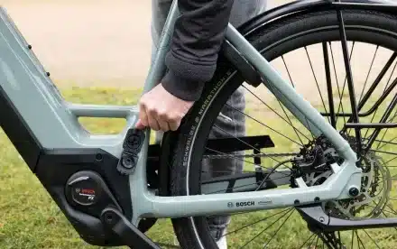 Nahaufnahme des Rahmens eines STEVENS E-Triton 7.8.1 Plus HT E-Bikes mit einer Hand, die eine Befestigungsvorrichtung für Zubehör nahe dem Hinterrad betätigt.