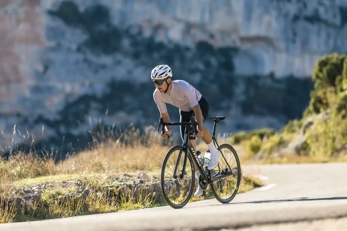 Sportlicher Radfahrer in voller Fahrt auf einem Stevens Izoard Pro Disc Rennrad auf einer asphaltierten Bergstraße, umgeben von üppiger Vegetation und Felsformationen.