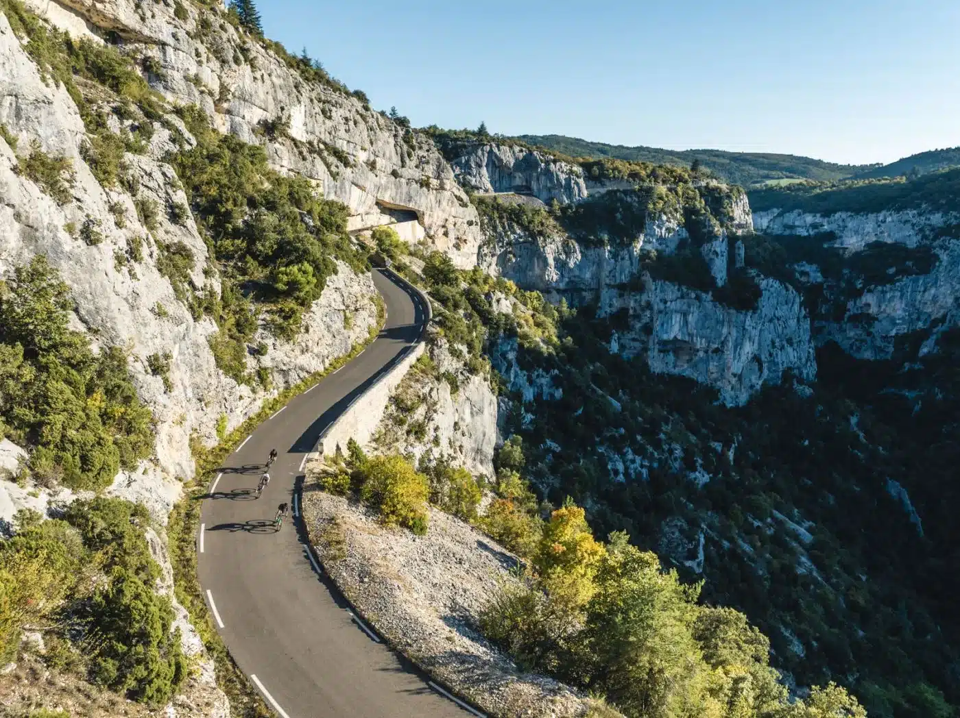 Gruppe von Rennradfahrern auf einer kurvenreichen Straße in einer bergigen Landschaft.
