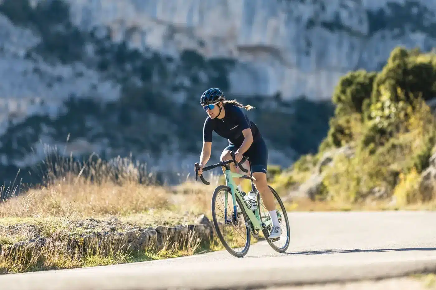 Radfahrerin fährt ein Stevens Izoard Pro Disc Rennrad auf einer asphaltierten Straße mit felsiger Berglandschaft im Hintergrund.