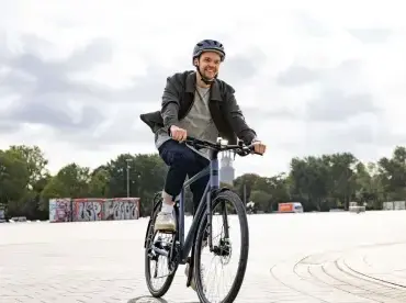 Mann mit Helm fährt ein blaues Stevens Kalea 6.1 HT Urban-Bike auf einem Platz.