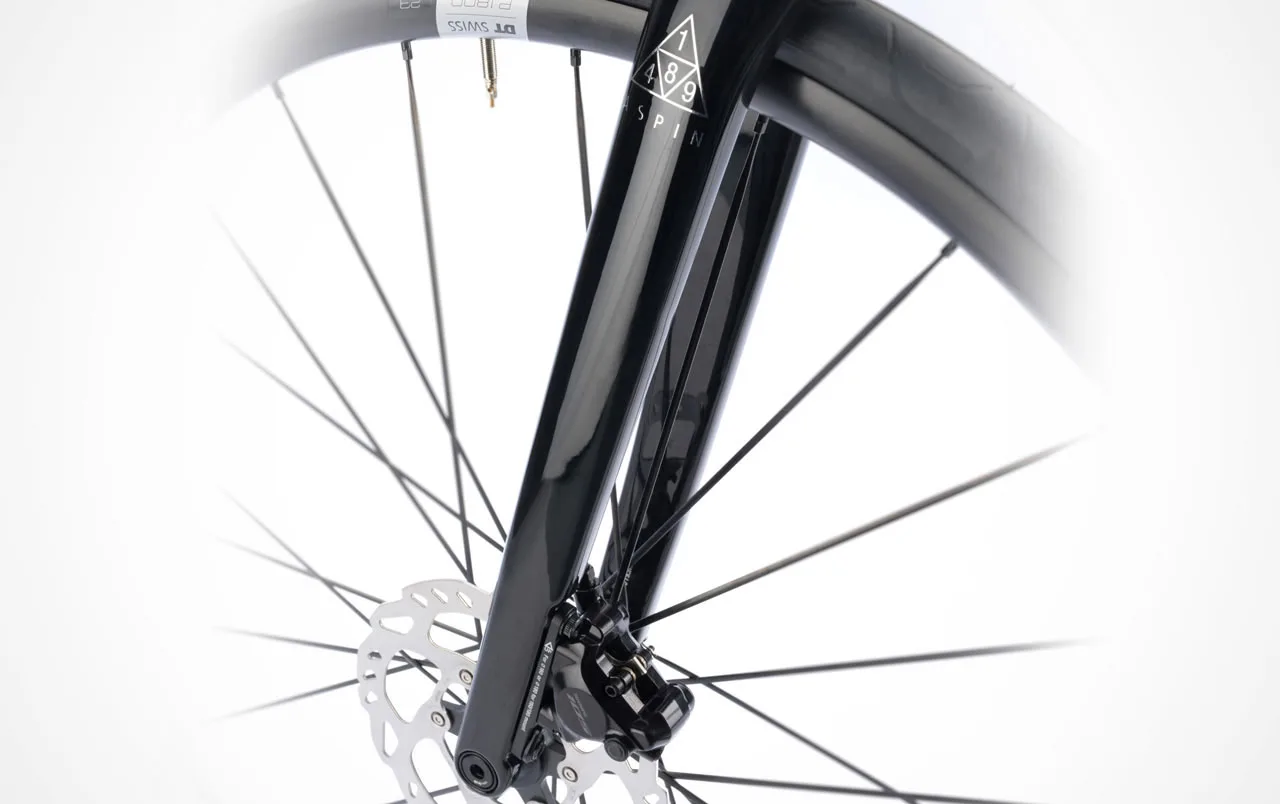 Nahaufnahme der schwarzen Carbon-Gabel, des Vorderrads mit DT Swiss Felge und Speichen, sowie der hydraulischen Shimano GRX Scheibenbremse des STEVENS Vapor 2x12 Cyclocrossers.