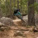 Mountainbikerin fährt auf einem staubigen Trail bergab, umgeben von Bäumen und Felsen.