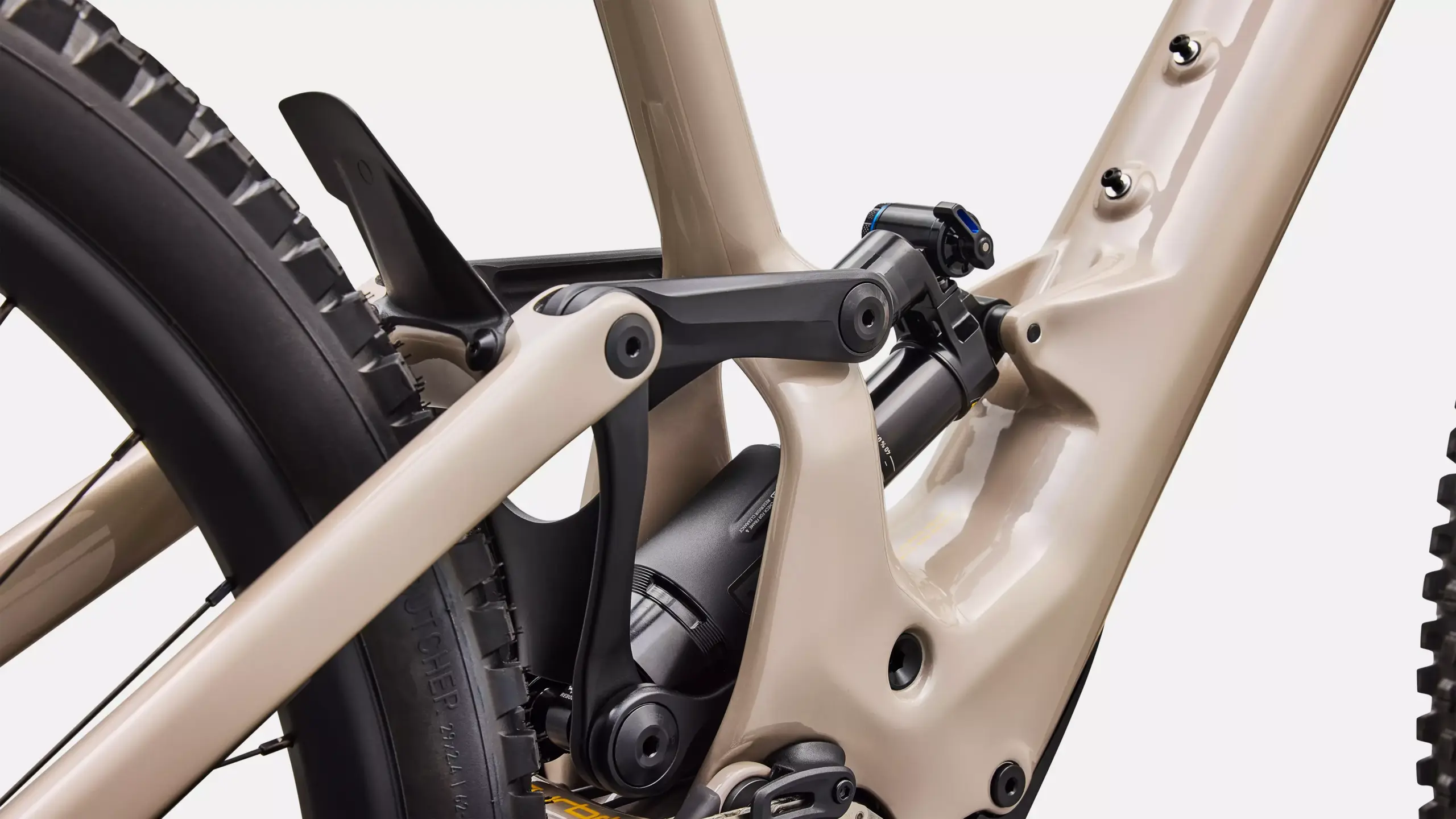 Nahaufnahme des Hinterbaus eines sandfarbenen E-Mountainbikes, das den Dämpfer und einen Teil des Hinterrads zeigt.
