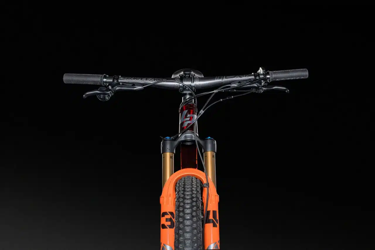 Detailansicht der Lenker- und Gabelpartie eines roten und orangefarbenen XRM 10.9 Mountainbikes vor schwarzem Hintergrund.