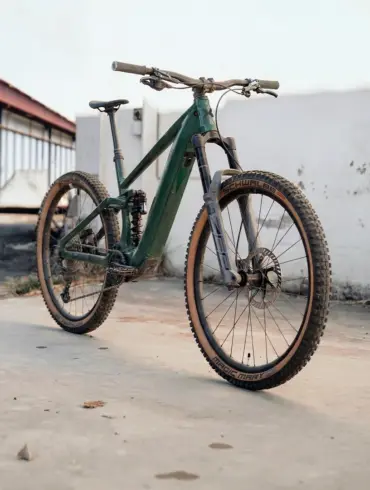 Seitenansicht eines dunkelgrünen Maxx Fab.4 Ela E-Enduro Fahrrads, das auf einem Betonboden steht.