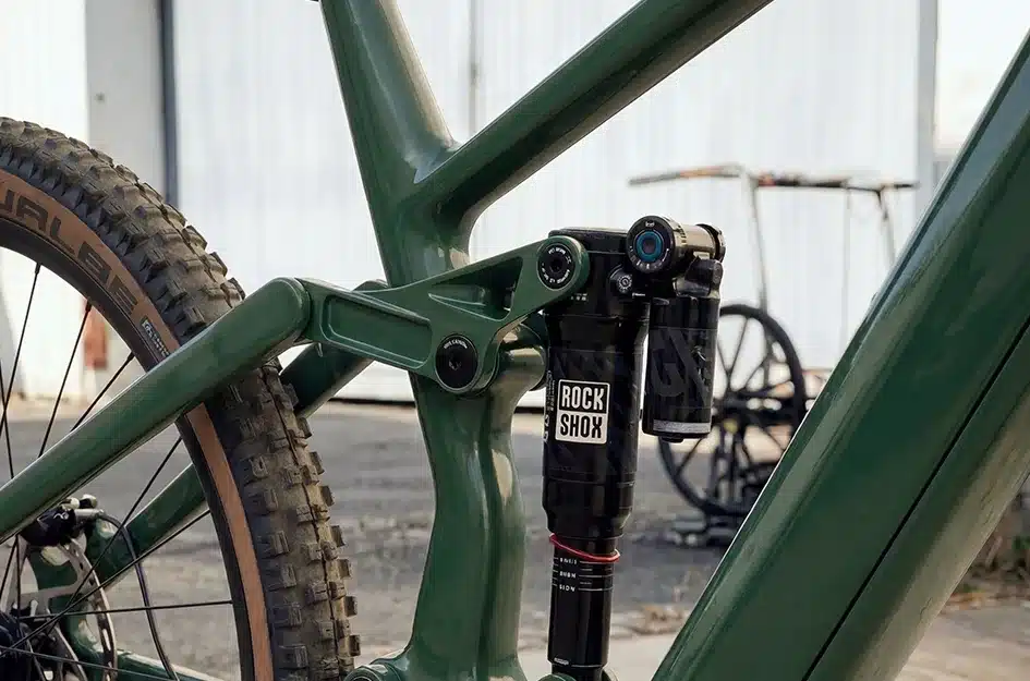 Detailansicht des grünen Carbon-Hinterbaus eines E-Enduro-Mountainbikes mit montiertem RockShox-Dämpfer und teilweisem Blick auf das Hinterrad.
