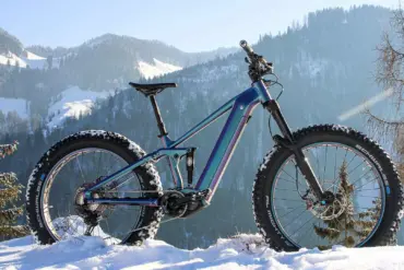 Vollgefedertes MAXX Huraxdax ELS X2 E-Mountainbike mit breiten Fatbike-Reifen steht im verschneiten Gelände mit Blick auf eine winterliche Berglandschaft.