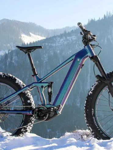 Vollgefedertes MAXX Huraxdax ELS X2 E-Mountainbike mit breiten Fatbike-Reifen steht im verschneiten Gelände mit Blick auf eine winterliche Berglandschaft.