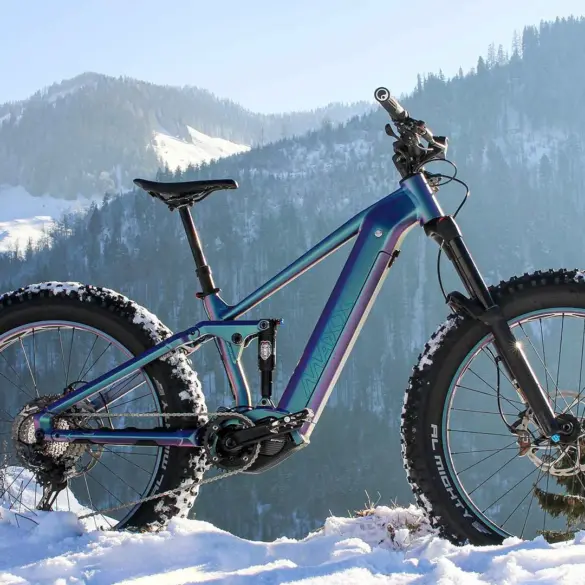 Vollgefedertes MAXX Huraxdax ELS X2 E-Mountainbike mit breiten Fatbike-Reifen steht im verschneiten Gelände mit Blick auf eine winterliche Berglandschaft.